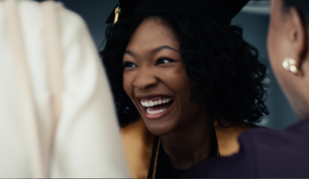 An African American female grins while surrounded by family at her graduation.