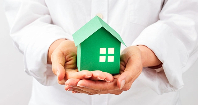 hands holding a small green paper house