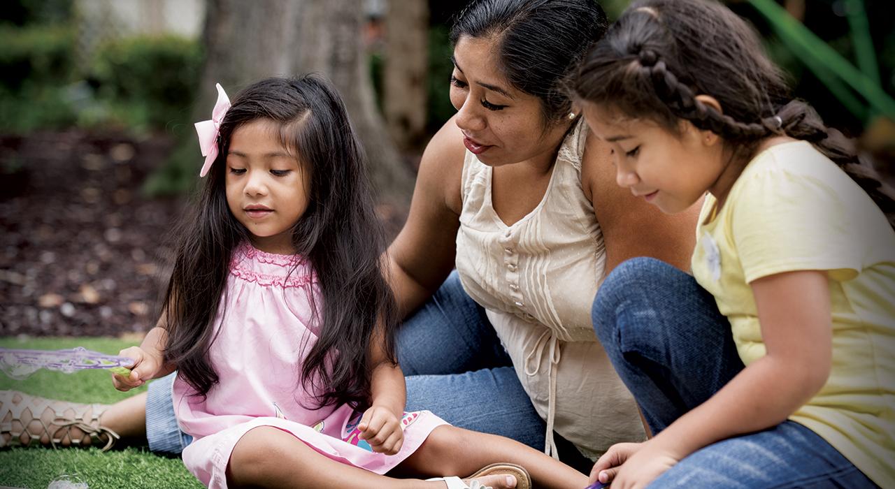 little girl blowing bubbles while mom and sister watch