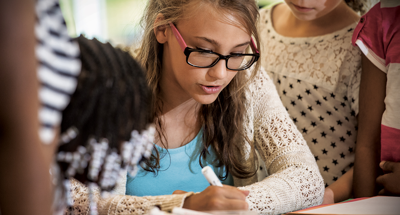 young blond youth girl writes something educational while wearing a sweater