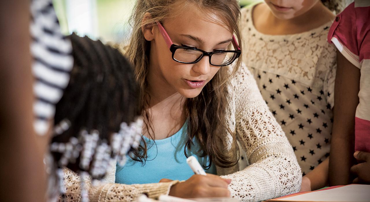 young blond youth girl writes something educational while wearing a sweater