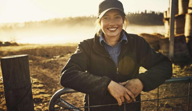 a female farmer stands at a gate in an image representing animal welfare