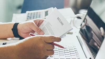 hand holding a printed resume infant of a laptop