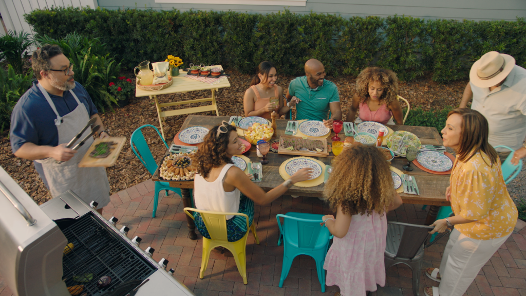 Large family gathering in backyard with fresh grilled food at a table.
