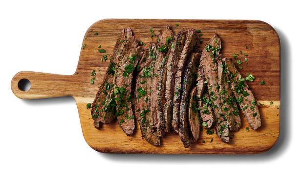 thin sliced steak garnished with cilantro on a carving board