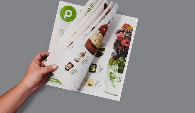 hand holding a Publix weekly ad flyer on a grey background