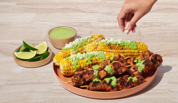 hand adding topping to Pork Skewers with Corn