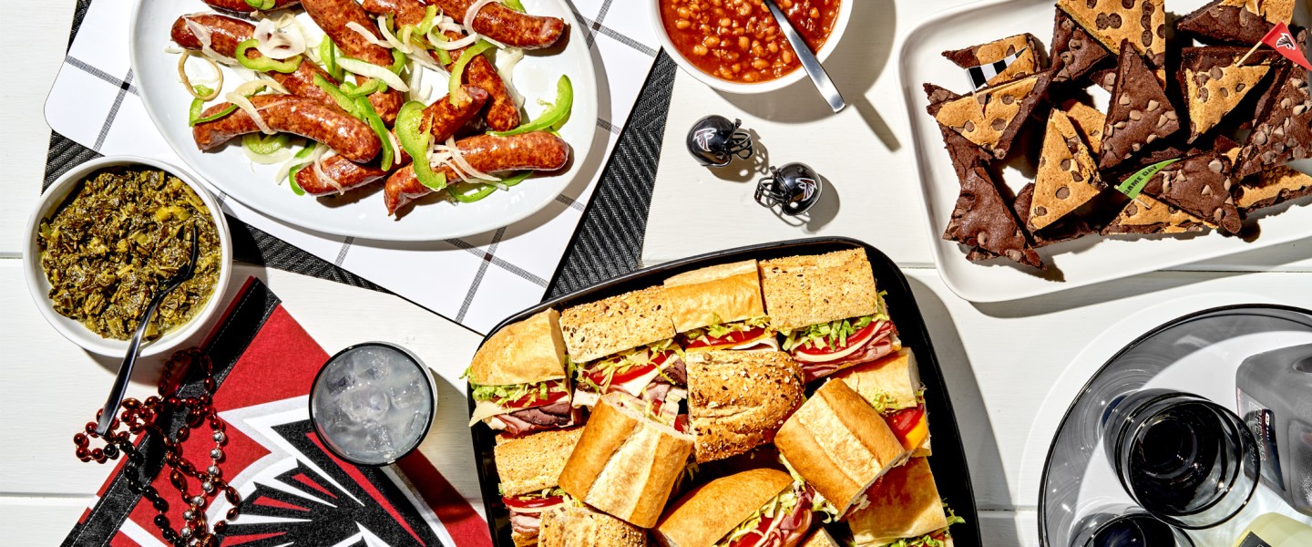 platters of subs, sausages, brownies, and bowls of dips and beans