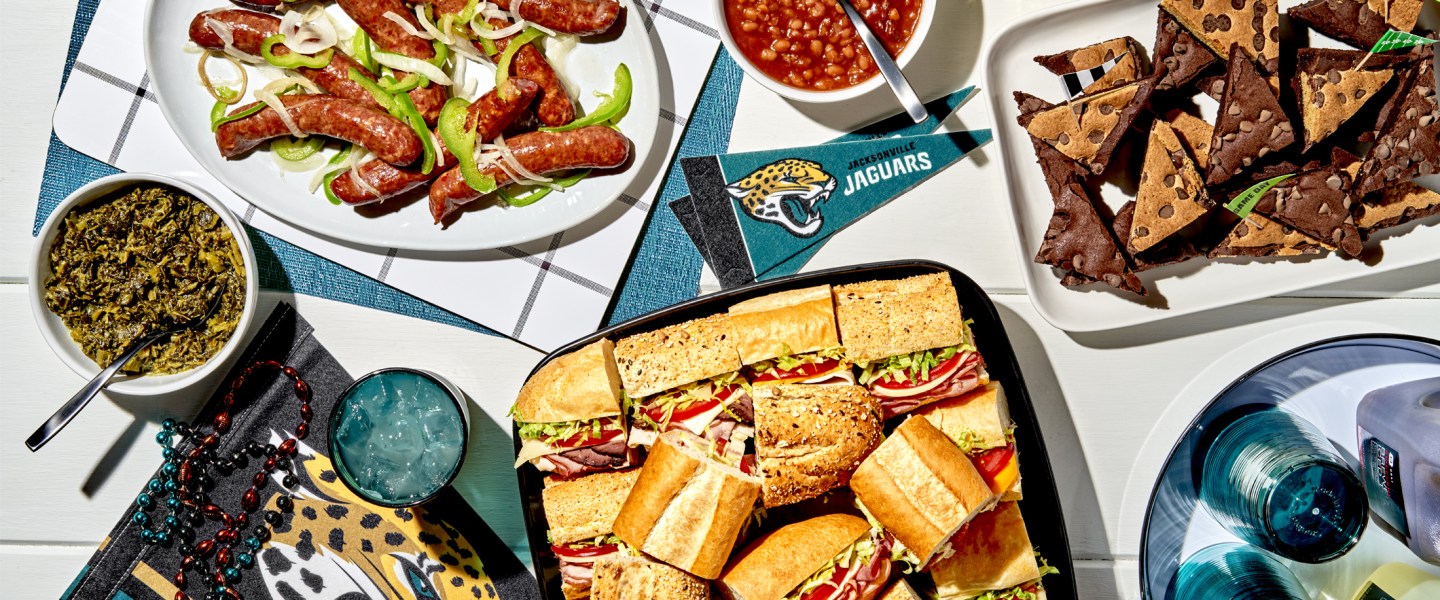 platters of subs, sausages, brownies, and bowls of dips and beans